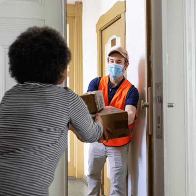Delivery man in hi-vis vest and fac mask handing over parcels to the customer